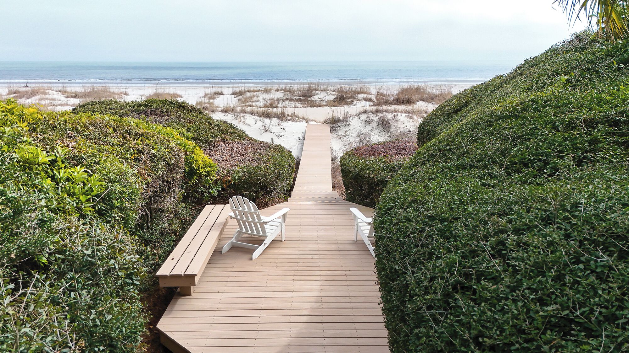 Un sendero de madera que lleva a sillas de playa con vista al océano.