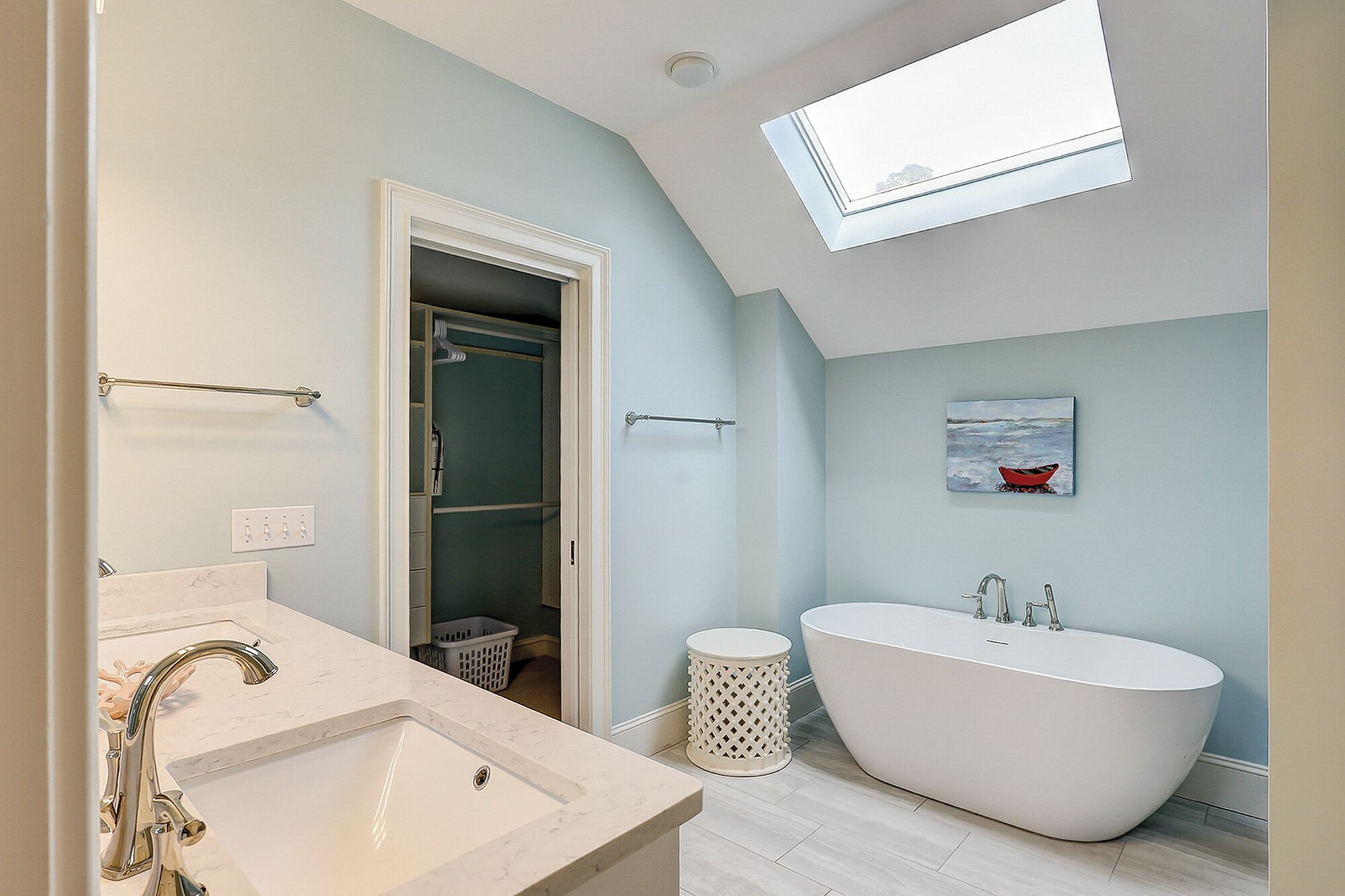 A modern bathroom with a freestanding bathtub, a walk-in closet, and a skylight.
