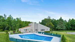 Et moderne hus med swimmingpool, omgivet af en velplejet græsplæne og træer.