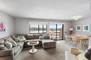 A living room with a sofa, ottoman, coffee table, and a dining area with chairs and a table. - 4BR Pool Access, Near Nubs Nob and Petoskey (Harbor Springs)
