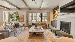 Un salón espacioso con chimenea, ventilador de techo y un ventanal con vistas a un balcón.