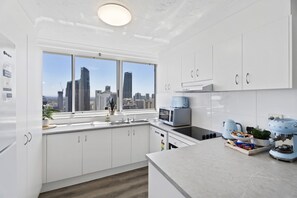 Eine moderne Küche mit weißen Schränken, einem großen Fenster mit Blick auf die Stadt, einem Einbauofen und einer Kaffeemaschine.