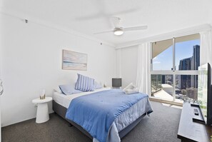 Ein Hotelzimmer mit einem Bett, einem kleinen Nachttisch, einem Schreibtisch mit Stuhl, einem Fernseher und einem großen Fenster mit Blick auf die Stadt.