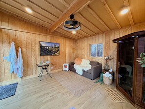 Una habitación acogedora con paredes de madera, un sofá gris, una pequeña mesa con un florero y una ventana.