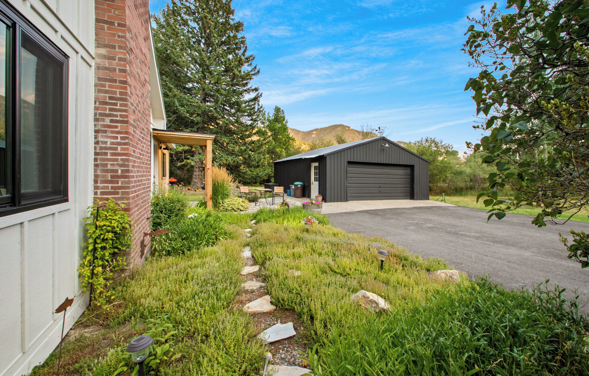 A residential property with a brick house, a wooden pergola, a garage, and a well-maintained garden with a stone pathway.