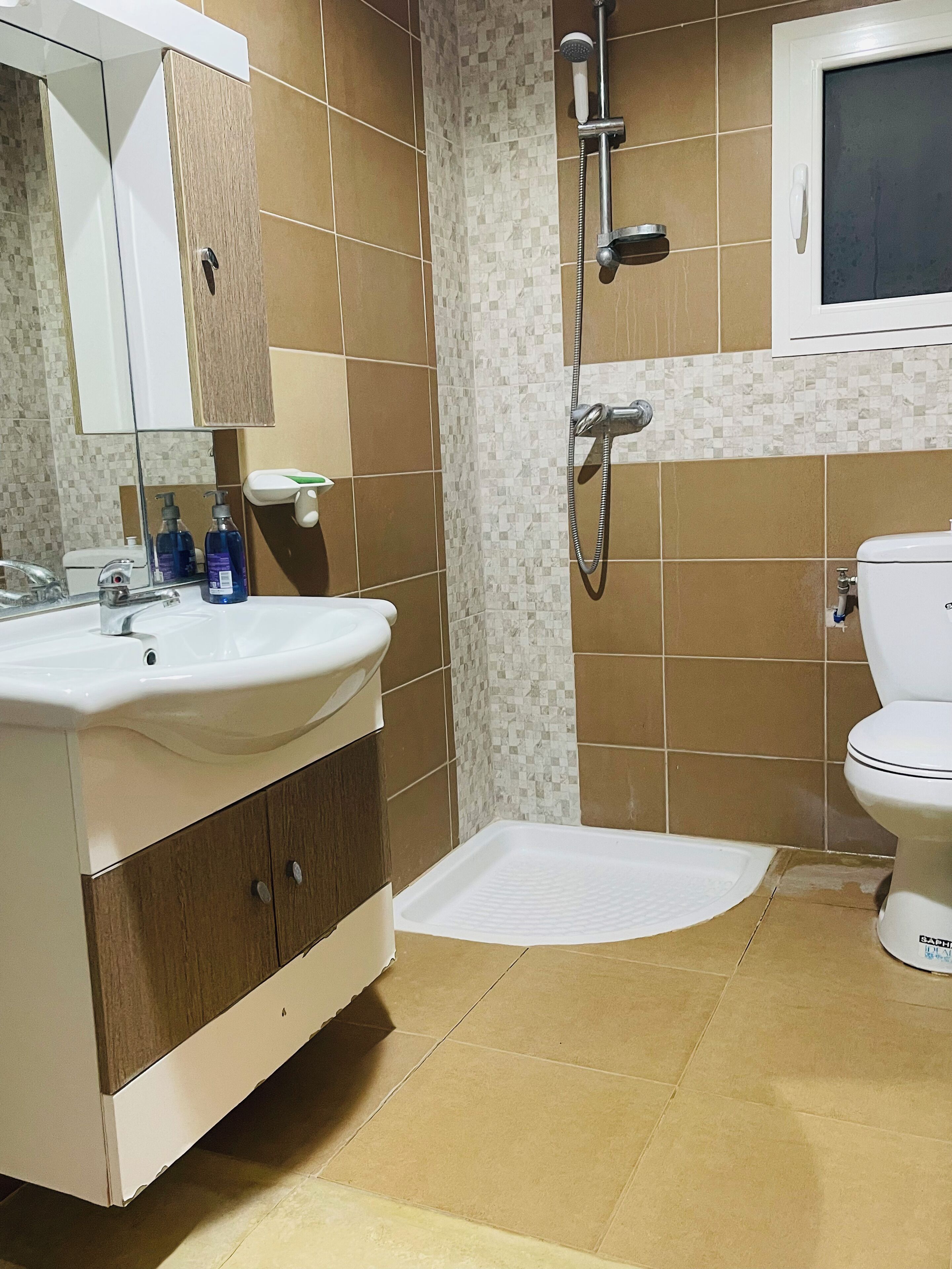 Un baño con lavamanos, espejo, ducha, inodoro y un ventanal.