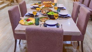 Un coin repas avec une table en marbre dressée pour le repas, entourée de chaises à l’assise recouverte d’un tissu violet.