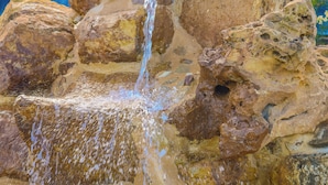 Une cascade artificielle en roche, avec de l’eau qui s’écoule sur les rochers et se déverse dans un bassin.