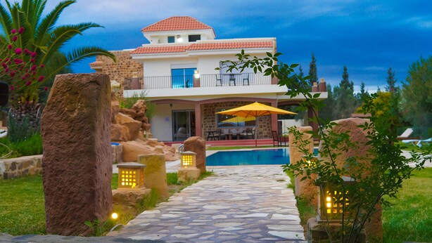Une maison moderne à deux étages, dotée d’une façade en pierre, d’une piscine et d’un chemin en pierre menant à l’entrée.