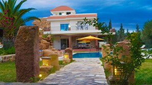 Una casa moderna de dos pisos con fachada de piedra, piscina y un camino de piedra que conduce a la entrada.