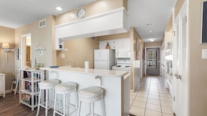 Una cocina con armarios blancos, una isla central con taburetes, un refrigerador y un microondas.