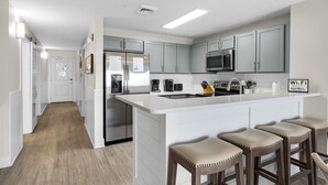 Una cocina moderna con armarios grises, un refrigerador de acero inoxidable, un microondas y una isla grande con taburetes de bar.