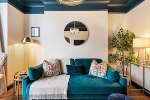 Un canapé de couleur turquoise agrémenté de coussins à motifs, un miroir rond et une plante en pot, le tout dans un salon moderne.