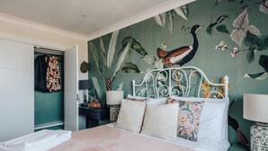 A bedroom with a bed, a nightstand, a lamp, and a wall with a bird and plant mural. - Cosy Family Apartment 2 min from Hyde Park (London)