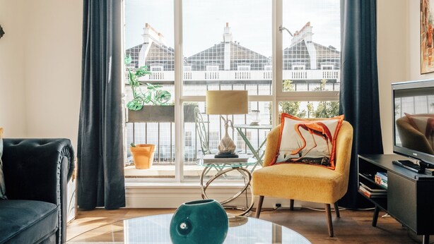 A living room with a glass coffee table, a yellow armchair, a black sofa, and a TV. - Cosy Family Apartment 2 min from Hyde Park (London)