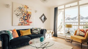 A living room with a black sofa, a glass coffee table, and a yellow armchair. There is a large window with a view of a building outside. - Cosy Family Apartment 2 min from Hyde Park (London)