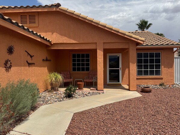 A house with a stucco exterior, a tiled roof, and a front porch with two chairs and a small table.