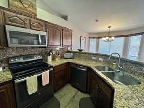 A kitchen with granite countertops, wooden cabinets, a built-in microwave, a toaster, and a stainless steel sink. - The Desert Rose | Ground-Level, Garage, 3BR + $510 in complimentary daily activities (Mesquite)