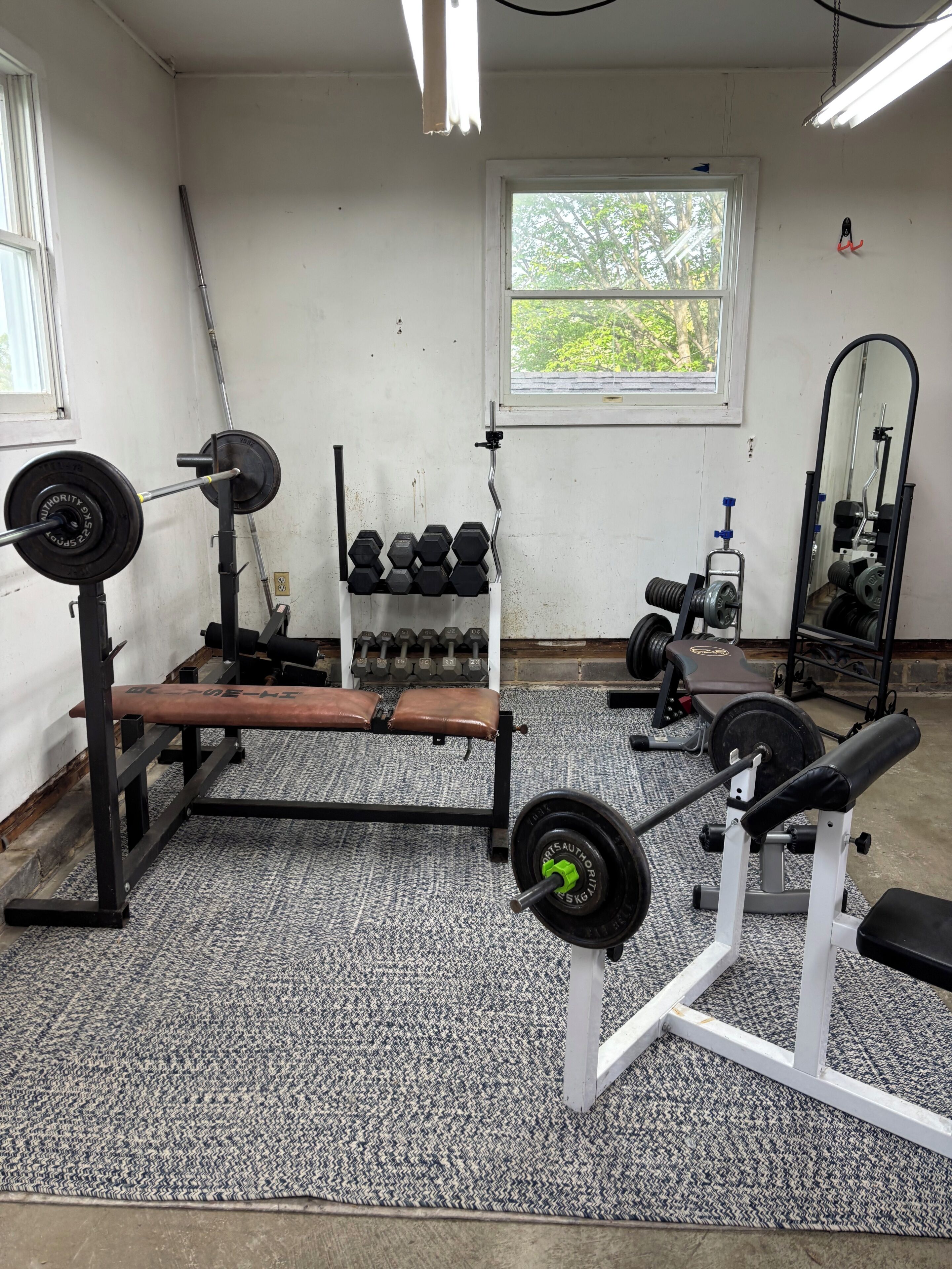 Un gimnasio con equipo de levantamiento de pesas, una banca y un espejo.
