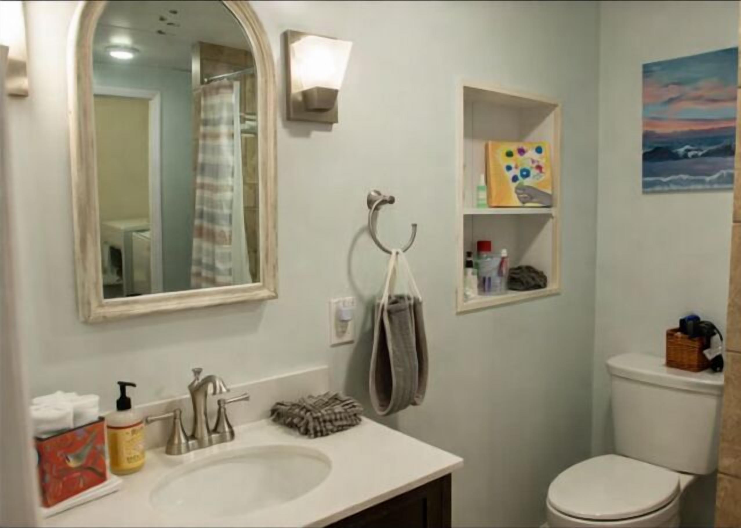 A bathroom with a sink, mirror, towel rack, toilet, and a shelf with toiletries.