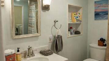 A bathroom with a sink, mirror, towel rack, toilet, and a shelf with toiletries.