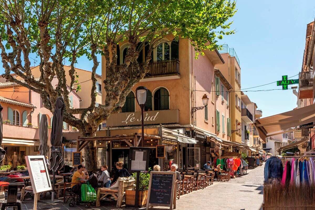 A street with outdoor seating, a café named 'Le Sud', and a clothing stall.