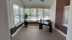 Una habitación con ventilador de techo, pared de ladrillo, ventana con persianas, planta en maceta y una mesa.