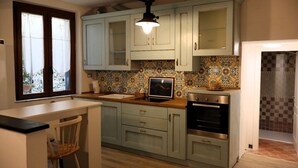 A kitchen with light blue cabinets, a tiled backsplash, a modern stove, and a dining area with a chair.