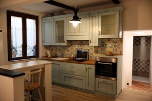 A kitchen with light blue cabinets, a tiled backsplash, a modern stove, and a dining area with a chair. - Portovenere Gem: Stay a stone's throw from St. Peter's Church ⚓, ✨, 🌊 (Portovenere)