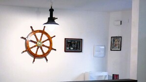 A room with a wooden ship's wheel, a black pendant light, a white counter, and two wooden chairs.