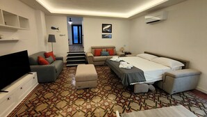 A hotel room with a TV, sofa, bed, and patterned carpet.