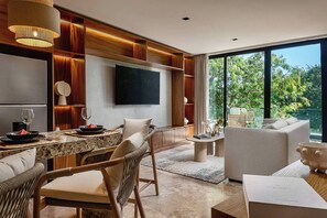 A modern living room with a dining area, a flat-screen TV mounted on the wall, wooden paneling, and large windows offering a view of greenery. - Beautiful 2-bedroom apartment "Casa Lumina" in Narai Aldea Zama by HEUSHAVEN, Tulum. Features a private terrace, full kitchen, fast WiFi, rooftop pool, gym, and shared amenities. Prime location between downtown Tulum and the beach road. (Tulum)