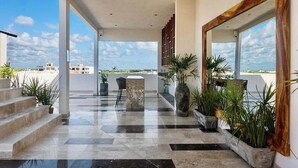 Amplo espaço interno com vista para o céu, com piso de mármore, escada e vários vasos de plantas.