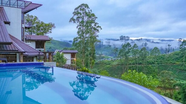 Ein modernes Hotel mit einem großen Infinity-Pool, der die umliegende Vegetation und Hügel widerzuspiegeln scheint.