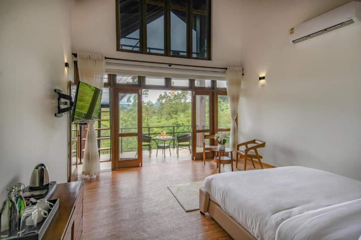 A bedroom with a large bed, a TV, a desk, and a balcony with a table and chairs.