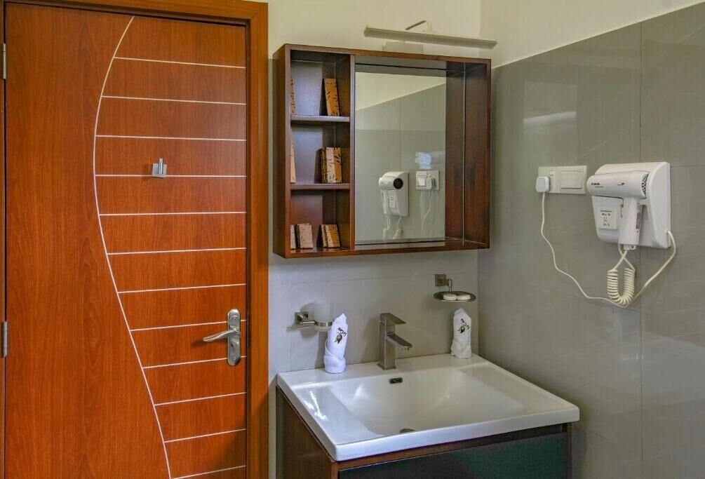 Un baño con puerta de madera, un lavamanos blanco, un espejo y un perchero para toallas.