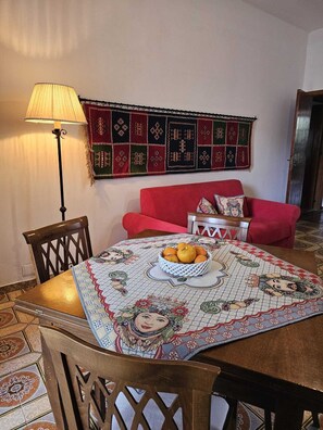 A dining area with a table set for two, a red sofa, a wall hanging, and a floor lamp. - Vacation home Villa Strazzeri a stone's throw from the sea (Palermo)
