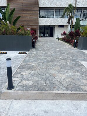 A paved pathway leading to a building with a stone facade and large windows. - Distrito Norte condo 1-bedroom in beautiful Cozumel with Large swimming pool (Cozumel)