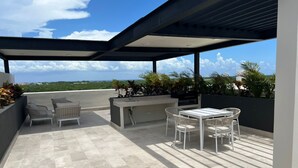 En tagterrasse med udendørs møbler, grill og udsigt over byens skyline.