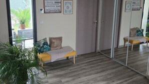 Una habitación con piso de madera, un sofá con cojines, un espejo grande y una puerta.