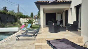 Un área junto a la piscina con sillas de descanso y un porche cubierto.