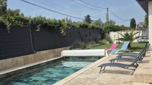 Una piscina con solárium de baldosas, sillas de descanso y un tobogán pequeño.