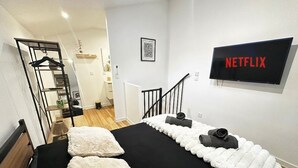 A bedroom with a bed, a black and white striped wall, a black TV, and a staircase. - T2 Duplex in hyper-centre - Quiet, independent access (Vienne)