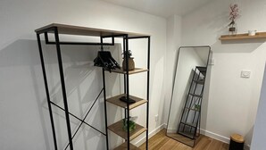 A compact room with a wooden floor, a metal-framed shelving unit, a small table with a lamp, and a mirror on the wall. - T2 Duplex in hyper-centre - Quiet, independent access (Vienne)