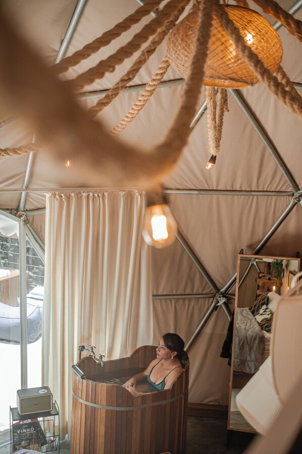 A wooden tub in a tented room with a window, a mirror, and a hanging light fixture.