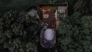 An aerial view of a secluded cabin surrounded by dense forest, featuring a circular seating area and a small deck with a fire pit.