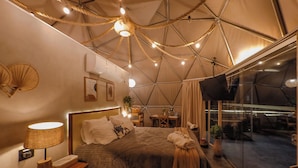 A tented accommodation room with a bed, bedside lamp, and a view of the outside.