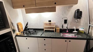 A compact kitchen with a gas stove, white cabinets, a wooden countertop, a sink, and a small wooden rack.