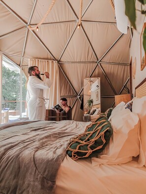 A tented room with a bed, a reading area, and a window with curtains.