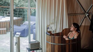 A tent with a wooden bathtub, a hot tub, and a glass door leading to an outdoor area with a hot tub and seating.